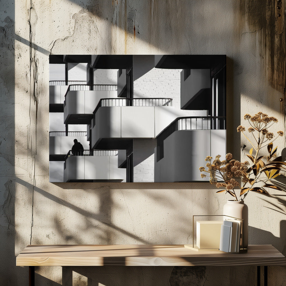A black and white architectural photograph of a modern building with repeating geometric balconies. Strong sunlight creates deep shadows, emphasizing the lines and curves of the structure. A lone silhouetted figure stands on one of the lower balconies. Decor