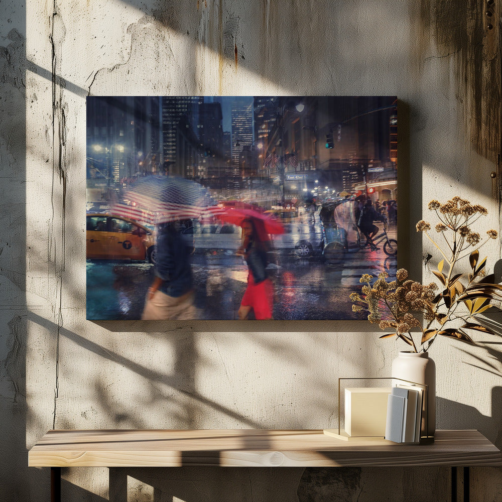 An artistic motion-blur photograph of a rainy night on East 42nd Street in New York City. Pedestrians with umbrellas, one with an American flag design and another bright red, cross the wet street as city lights and a yellow taxi reflect on the pavement, creating a vibrant, impressionistic scene within a silver frame. Decor
