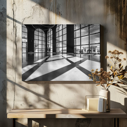 A striking black and white photograph of a spacious, modern hall with a polished floor. Dramatic shadows from large, arched windows are cast across the floor. Through the windows, a view of a classical European city with a triumphal arch can be seen. Print