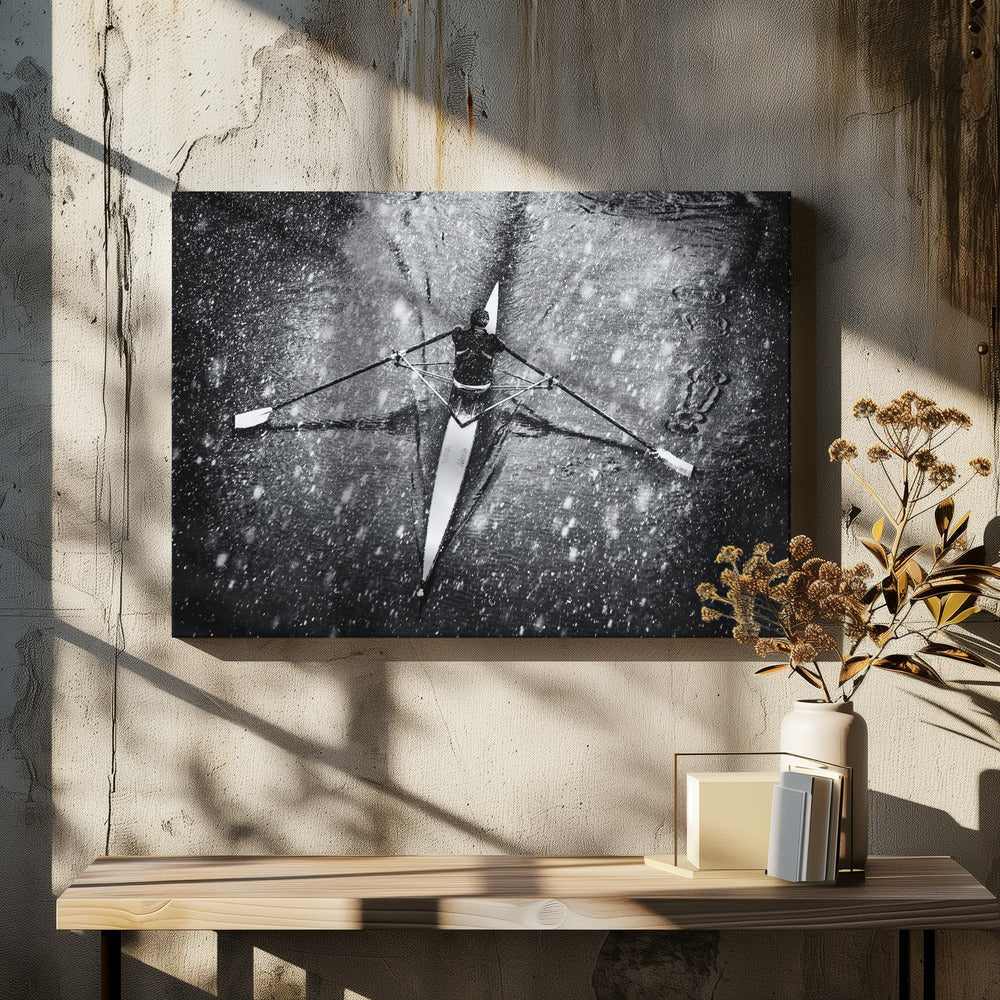 A dramatic black and white overhead photograph of a single rower in a narrow scull, captured mid-stroke as they cut through dark water during a heavy snowfall, creating a high-contrast and atmospheric scene. Decor