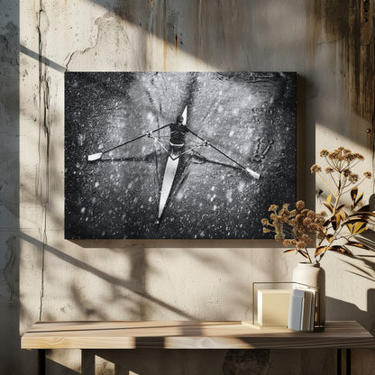 A dramatic black and white overhead photograph of a single rower in a narrow scull, captured mid-stroke as they cut through dark water during a heavy snowfall, creating a high-contrast and atmospheric scene. Decor