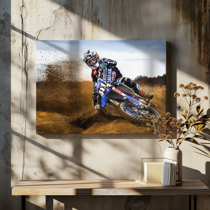 A motocross rider in full gear leans sharply into a turn on a dirt track, kicking up a large spray of mud and dirt from their blue and white Yamaha motorcycle. Artwork