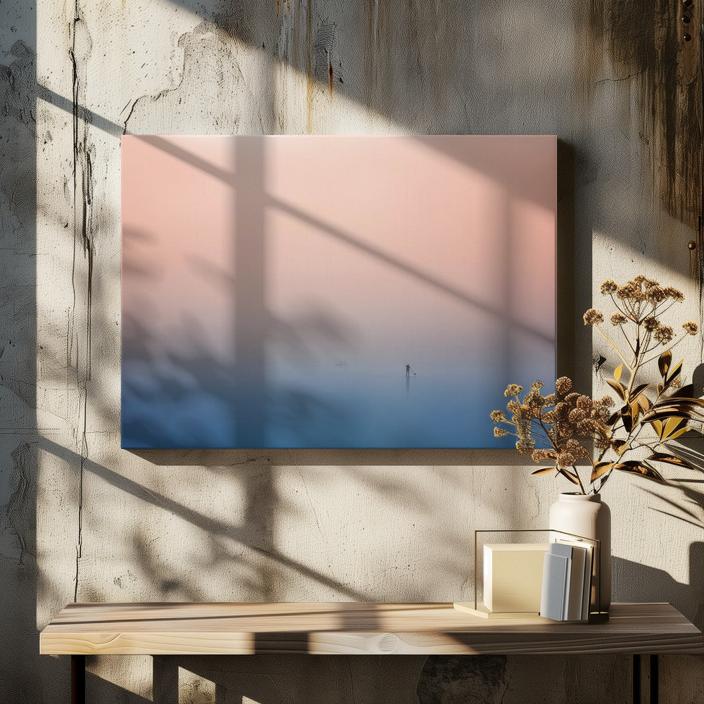 A minimalist framed photograph of a solitary person on a stand-up paddleboard, silhouetted against a vast, calm expanse of water under a hazy, gradient sky that shifts from soft pink to deep blue. Wall Art
