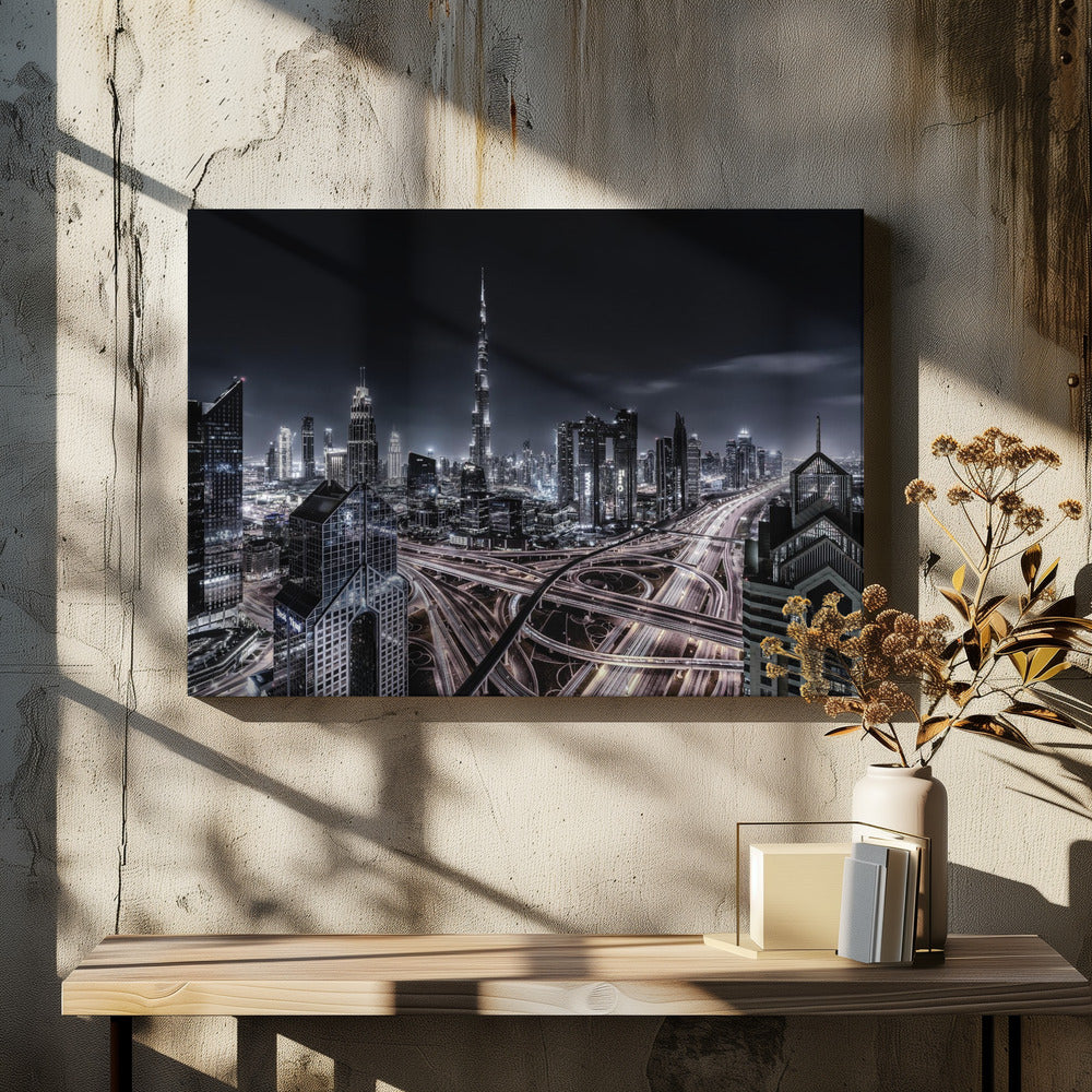 A striking black and white aerial photograph of the Dubai skyline at night, captured in a silver frame. The Burj Khalifa stands tall in the background, while a complex web of illuminated highway overpasses and light trails from traffic fills the foreground, creating a dynamic and futuristic cityscape. Print