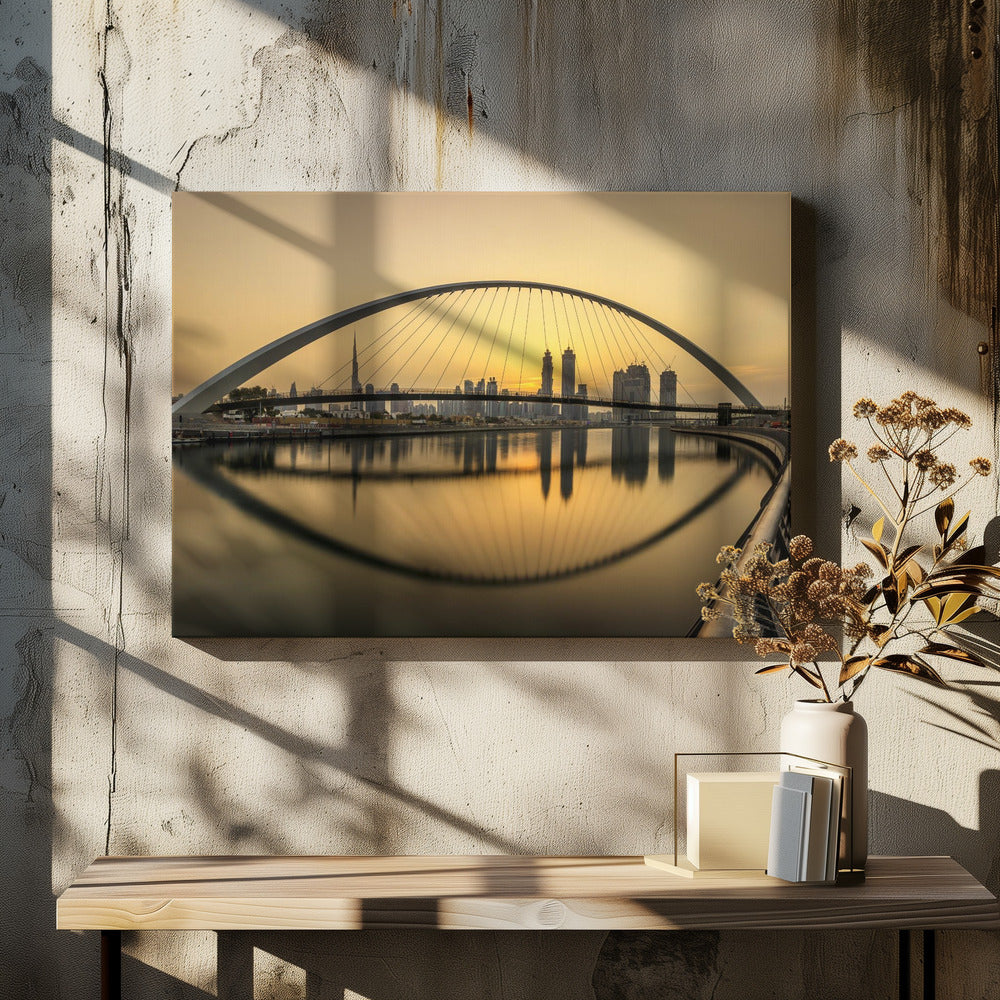 A sweeping view of the Dubai Water Canal Bridge at sunset, its white arch and cables stretching over the calm water. The city skyline, including the Burj Khalifa, is silhouetted against the golden sky, with the entire scene creating a perfect reflection in the water below. Print