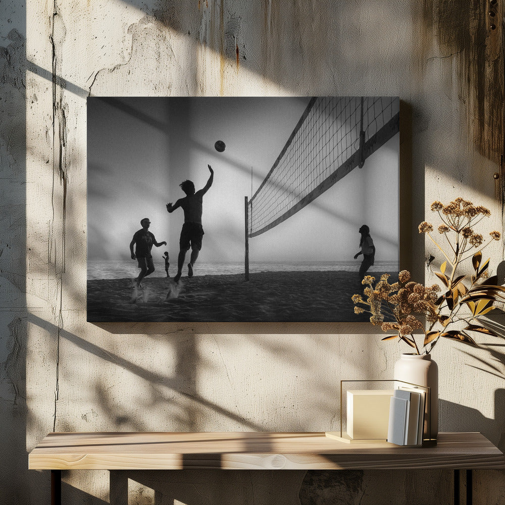 A black and white action shot of people playing volleyball on a beach, presented in a silver frame. The scene is silhouetted against a light sky, likely during sunrise or sunset. One player is captured mid-jump, arm raised to hit the ball over the net. Other players are visible on the sand, with the ocean in the background. Decor