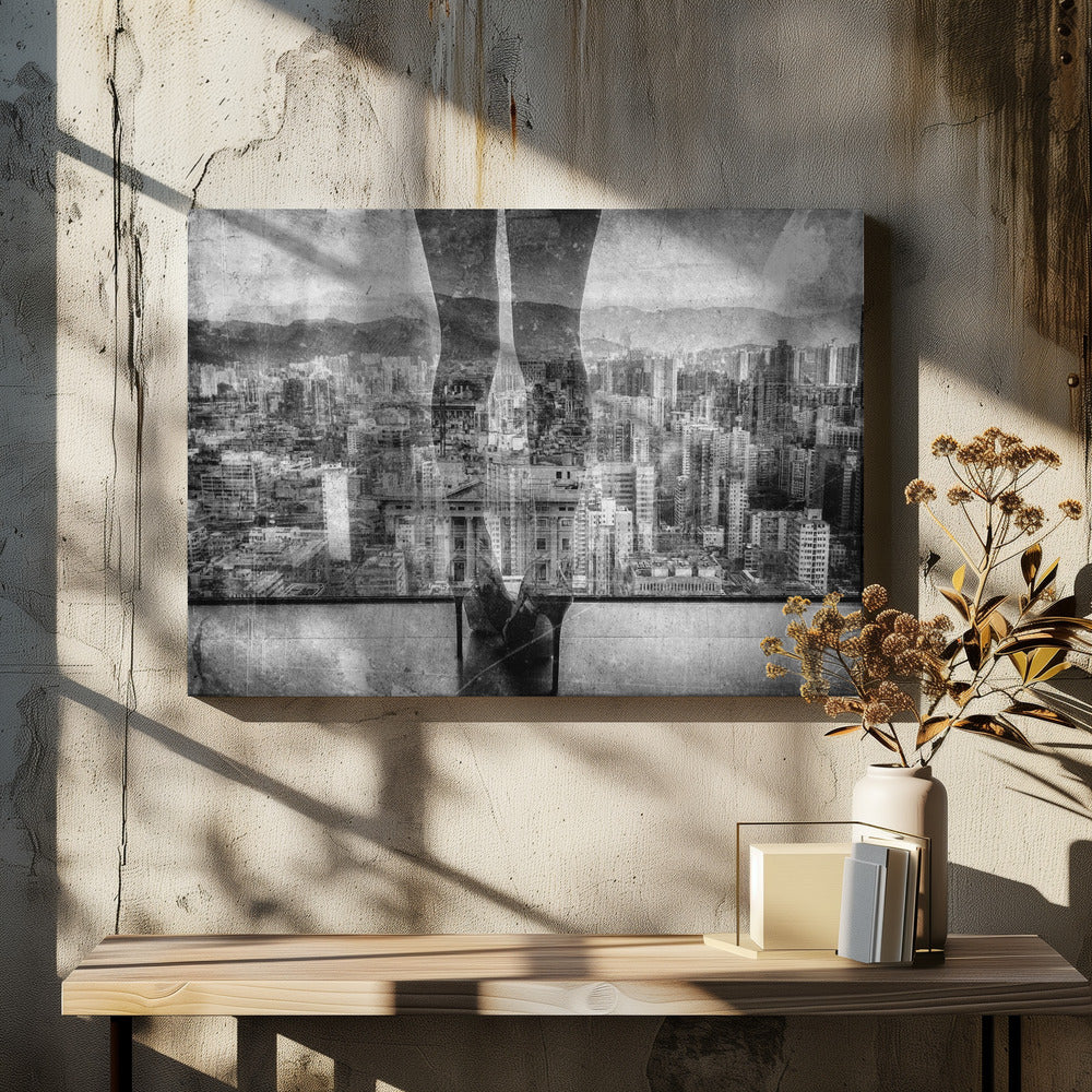 A framed, black and white artistic photograph featuring a double exposure. A vast, dense cityscape with distant mountains is visible through the translucent silhouette of a person's legs standing on a balcony edge. Poster