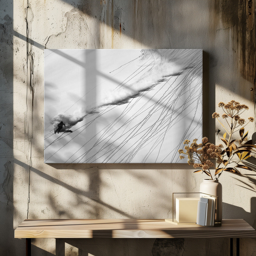 A dramatic black and white overhead photograph of a skier carving down a steep, powder-filled mountain slope, kicking up a huge plume of snow. Numerous ski tracks crisscross the pristine white snow, creating a pattern of dark lines. Poster