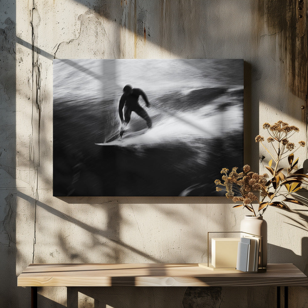 A dynamic black and white photograph of a surfer in a wetsuit carving through a wave. The image uses motion blur to emphasize the speed and energy of the water, creating a powerful and artistic effect. The artwork is presented in a simple silver frame. Print