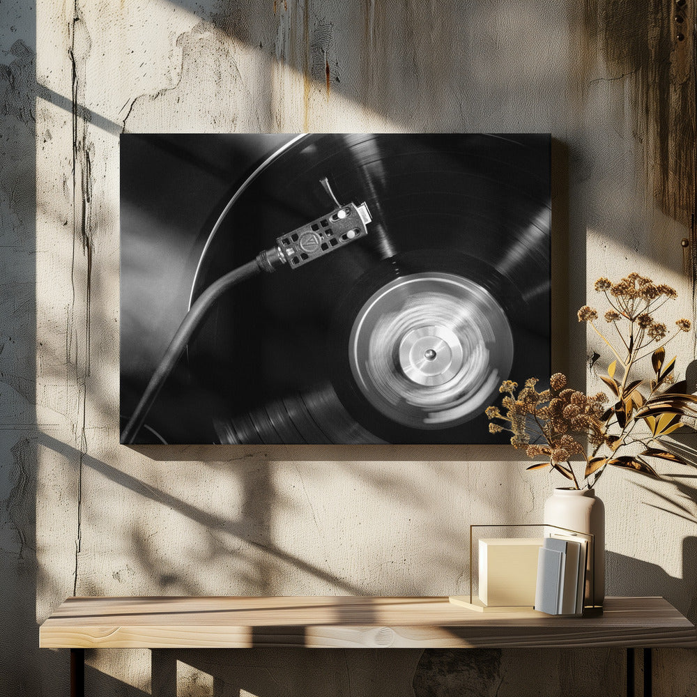 A framed, black and white, close-up photograph of a record player in action. The turntable is spinning a vinyl record, creating a motion blur on the center label. The tonearm and stylus are positioned over the grooved surface of the record. Poster
