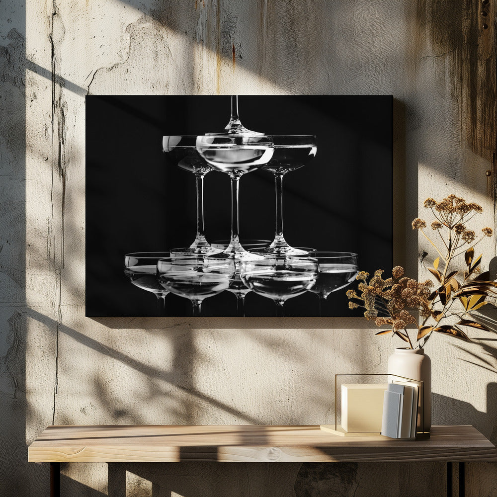 A black and white photograph of a champagne tower made of coupe glasses stacked in a pyramid shape against a solid black background, all within a silver frame. Print