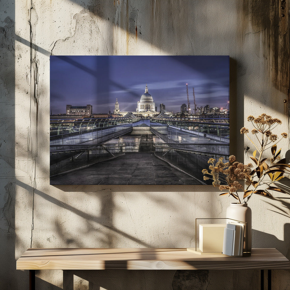 A nighttime photograph from the Millennium Bridge leading towards the brightly illuminated St. Paul's Cathedral against a dark blue twilight sky in London, all enclosed in a silver frame. Poster