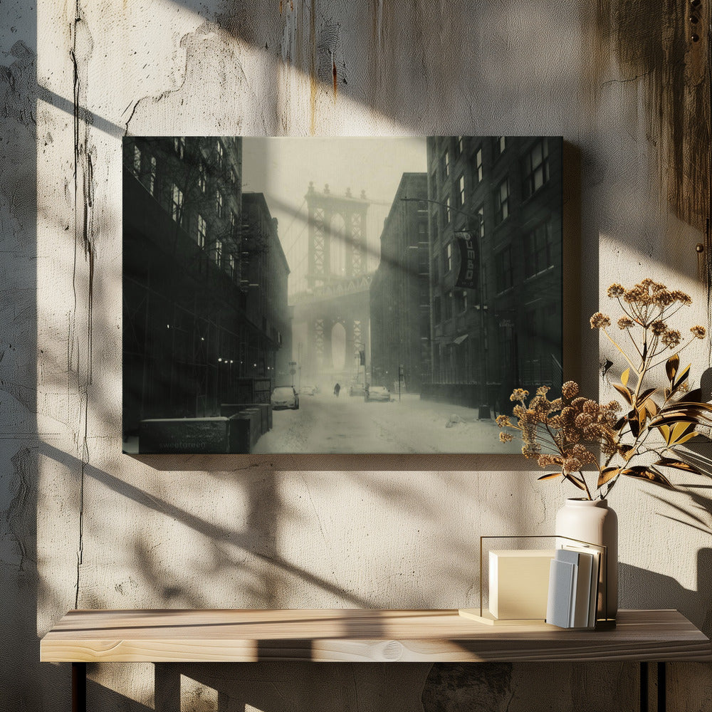 A framed, vintage-style black and white photograph capturing a snowy day in DUMBO, Brooklyn. The view looks down a snow-covered street lined with dark buildings, perfectly framing the Manhattan Bridge in the foggy distance. A few cars are parked along the street, and snow is visibly falling, creating a quiet, atmospheric winter scene. Decor