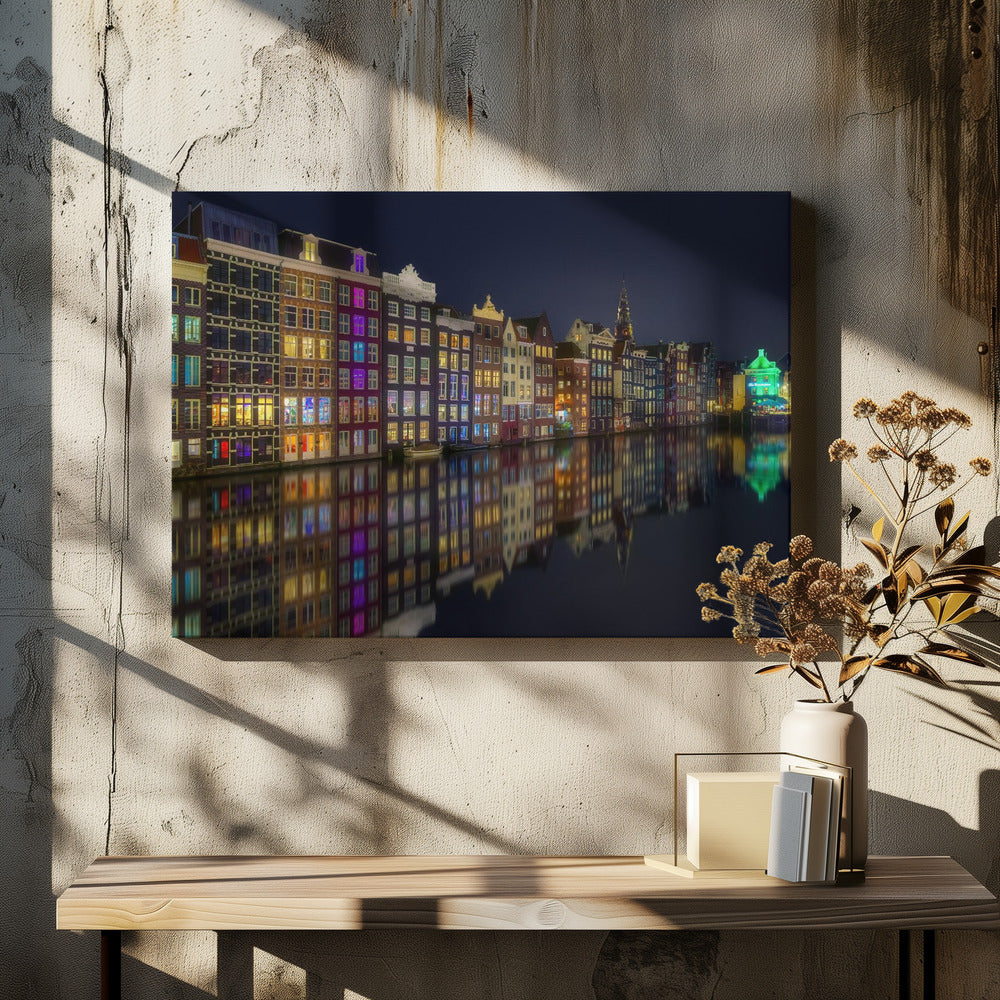 A vibrant nighttime photograph of colorful canal houses in Amsterdam, with their glowing lights beautifully reflected in the still water of the canal below, all framed in silver. Print