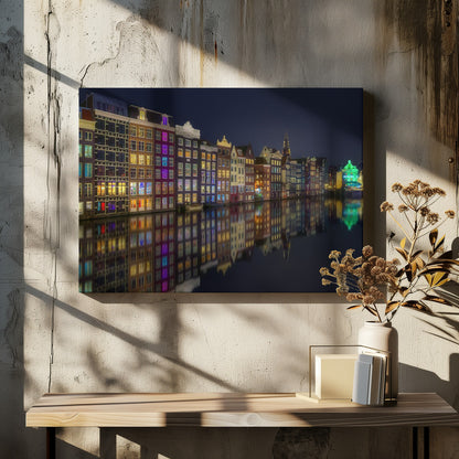 A vibrant nighttime photograph of colorful canal houses in Amsterdam, with their glowing lights beautifully reflected in the still water of the canal below, all framed in silver. Print