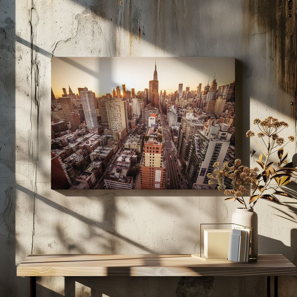An aerial photograph of the New York City skyline at sunset, with the Empire State Building prominent against the glowing sky. The warm light of the setting sun bathes the dense urban landscape in a golden hue. The entire scene is enclosed in a silver, brushed metal frame. Print