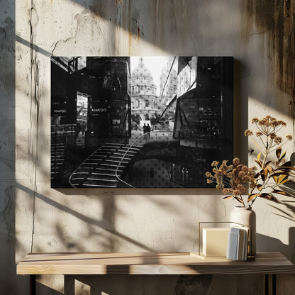 A framed, black and white photograph capturing a layered urban scene. The view, seen through a window with reflections of a curved, lit staircase, shows two people walking towards a large domed cathedral framed by modern glass buildings. Wall Art