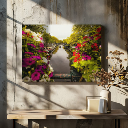 A scenic view looking down a canal in Amsterdam from a bridge, framed by vibrant, out-of-focus purple, red, and white flowers in the foreground. The canal is lined with houseboats and lush green and yellow trees, with historic buildings visible behind them. Poster