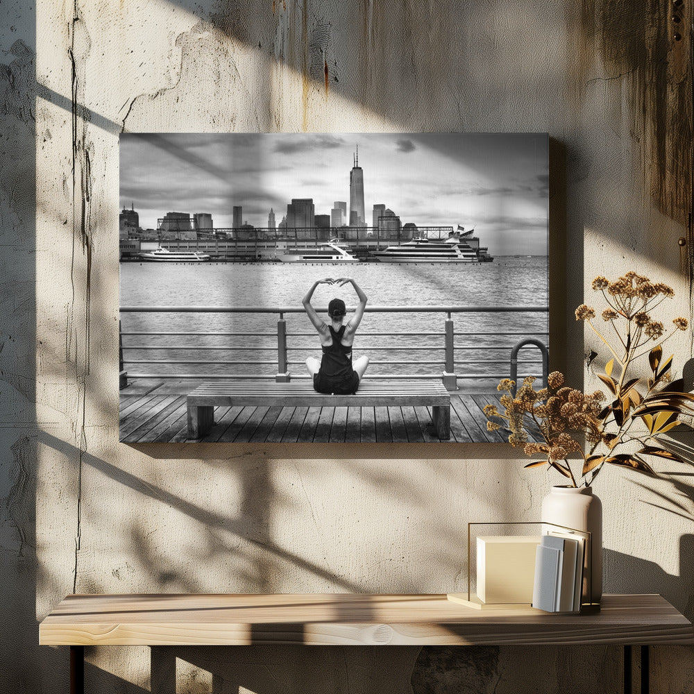 A framed black and white photograph showing the back of a woman sitting on a wooden bench on a pier. She is in a yoga pose with her arms raised, looking out at the Lower Manhattan skyline, including the Freedom Tower, across the water. Decor