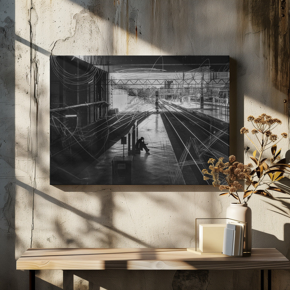 A framed, high-contrast black and white photograph of a person sitting alone on a deserted train platform, with tracks stretching into the distance. The entire scene is overlaid with frenetic white scribbles, creating an abstract and moody effect. Artwork