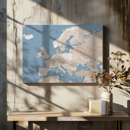 A detailed, framed map of Europe with a muted color palette. The oceans and seas are a soft blue, while the countries are various shades of beige and tan. Text labels for countries, cities, and bodies of water are clearly visible across the map. The map is housed in a simple silver-gray frame. Poster