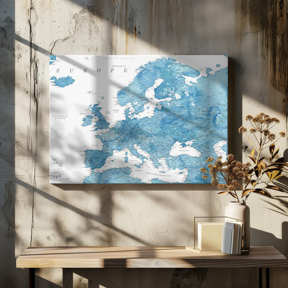 A framed map of Europe with a blue watercolor texture. The land is depicted in various shades of blue, while the oceans are white. Countries, cities, and bodies of water are labeled in black text. The map is housed in a simple, light gray frame. Poster