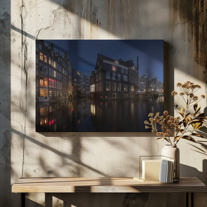 A framed photograph capturing a serene night view of an Amsterdam canal. Traditional Dutch houses with lit windows line the calm water, casting warm reflections under a deep blue twilight sky. Wall Art
