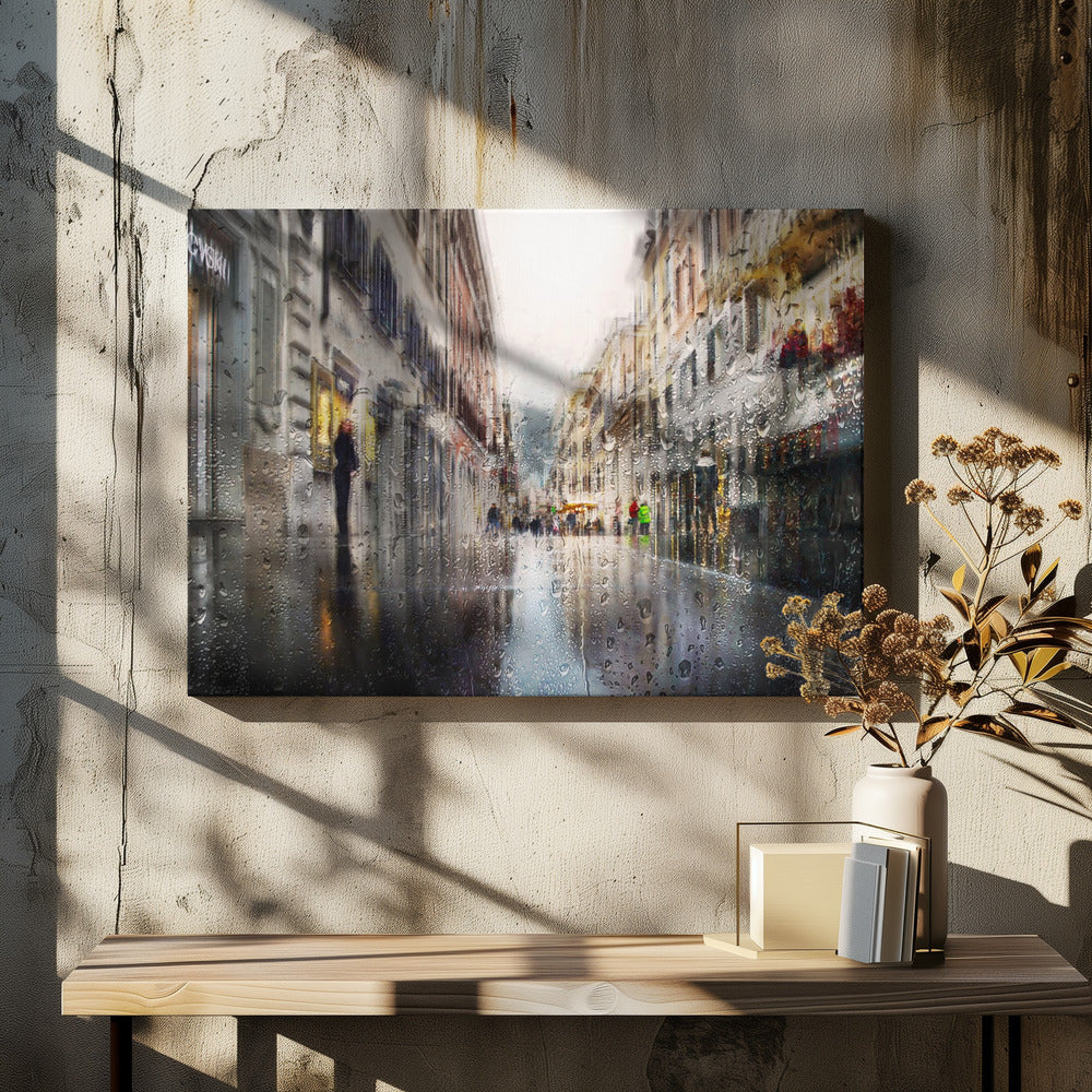 An impressionistic painting of a city street on a rainy day, viewed as if through a window covered in water droplets. The scene is blurred and atmospheric, with the wet pavement reflecting the muted colors of the buildings and distant figures. The artwork is presented in a silver frame. Decor