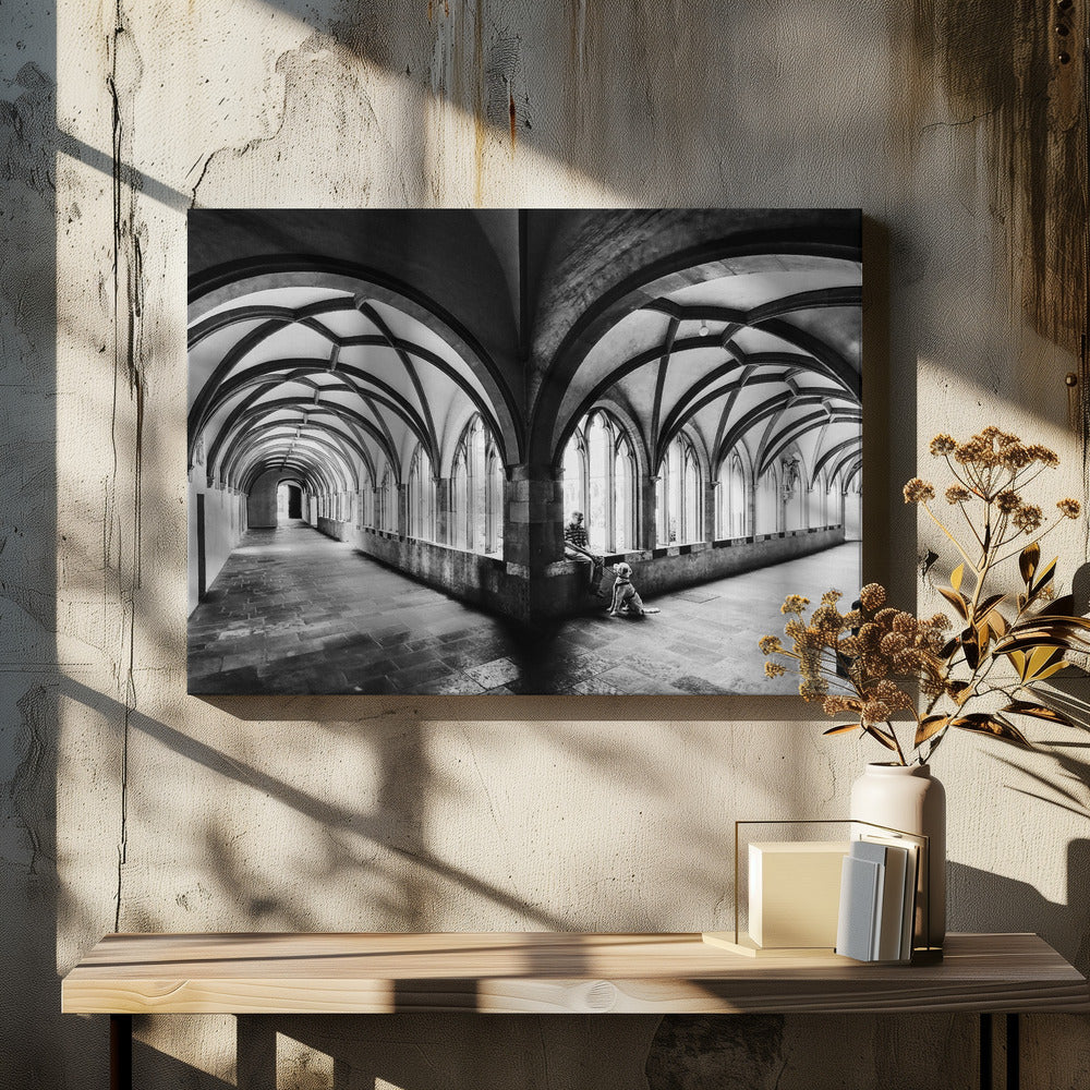 A black and white photograph of a person and their dog sitting in the corner of a Gothic cloister. The stone hallway features a dramatic vaulted ceiling and a long row of arched windows, creating a powerful sense of perspective and light. Decor