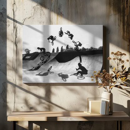 A dynamic black and white action shot showing the progression of a BMX rider doing a backflip off a large ramp. Multiple exposures capture the rider at different points in the air, creating an arc of motion against a bright sky. Strong shadows are cast on the ramp below. Print