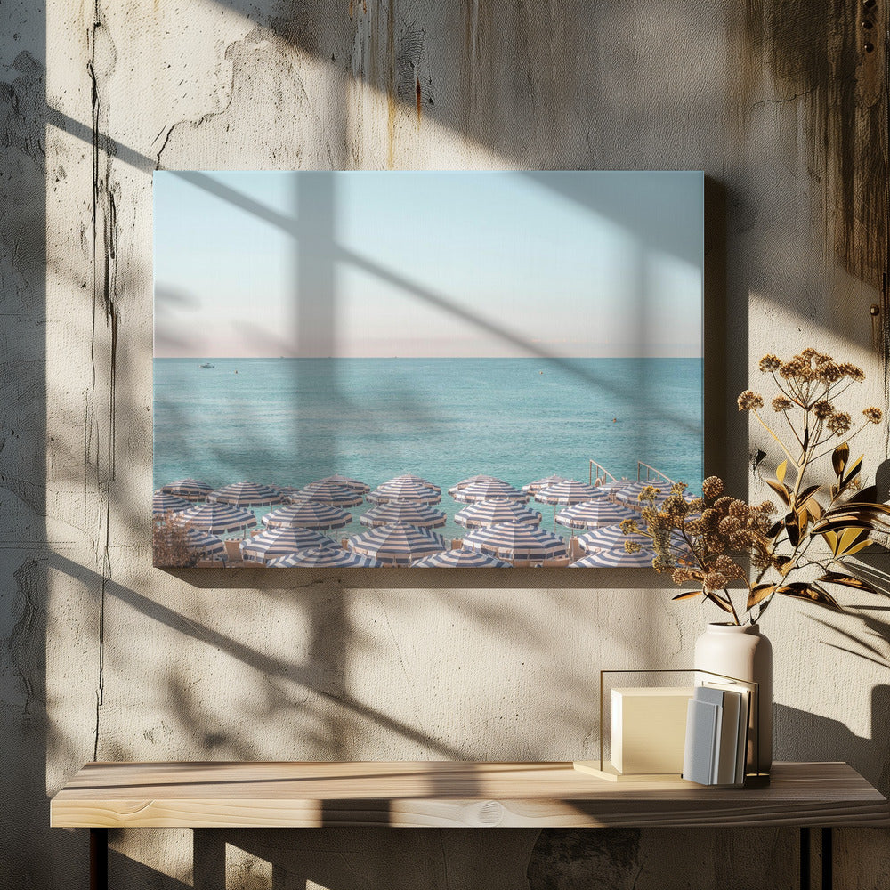 A high-angle photograph of a beach packed with blue and white striped umbrellas, with the turquoise ocean stretching out to a pale blue sky in the background. The entire image is enclosed in a silver frame. Poster