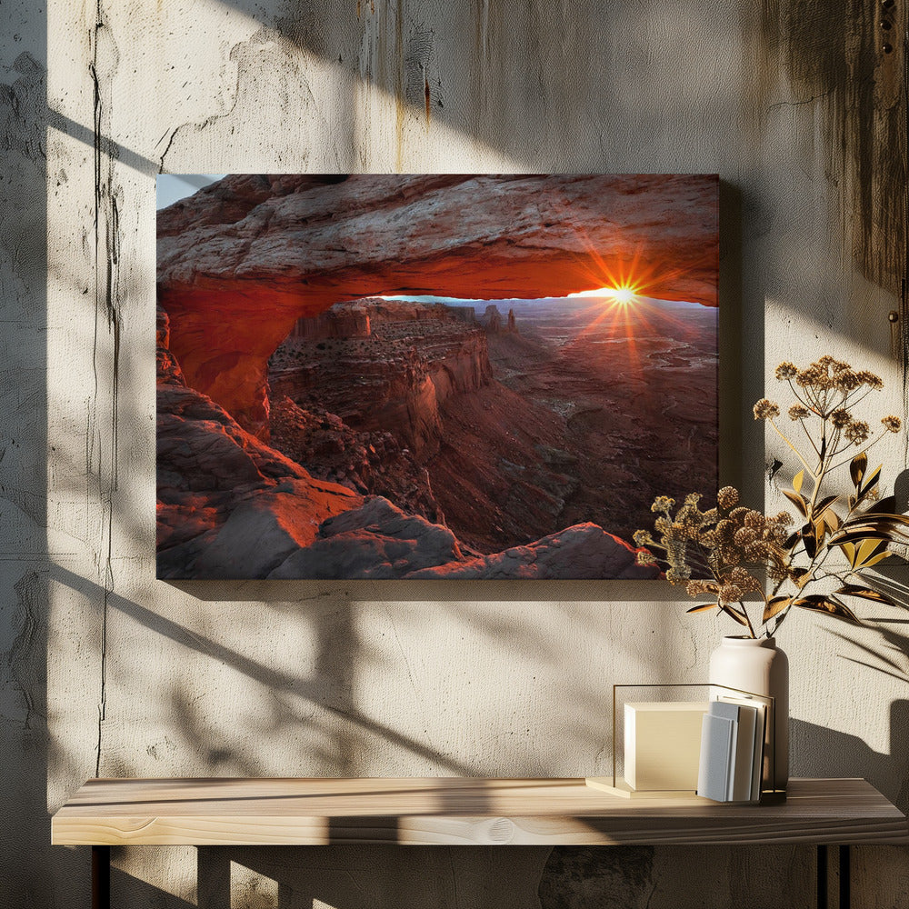 A spectacular sunrise seen through the natural frame of Mesa Arch in Canyonlands National Park, Utah. The sun bursts over the horizon, casting a dramatic orange and red glow on the underside of the rock arch and the vast canyon landscape below. Poster