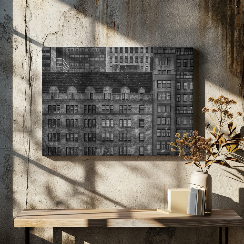 A dense, black and white photograph of various city buildings packed closely together. The image highlights the contrasting architectural styles, from an older stone building with a dark roof in the foreground to taller brick and modern glass buildings in the background, creating a geometric pattern of windows and textures. Decor