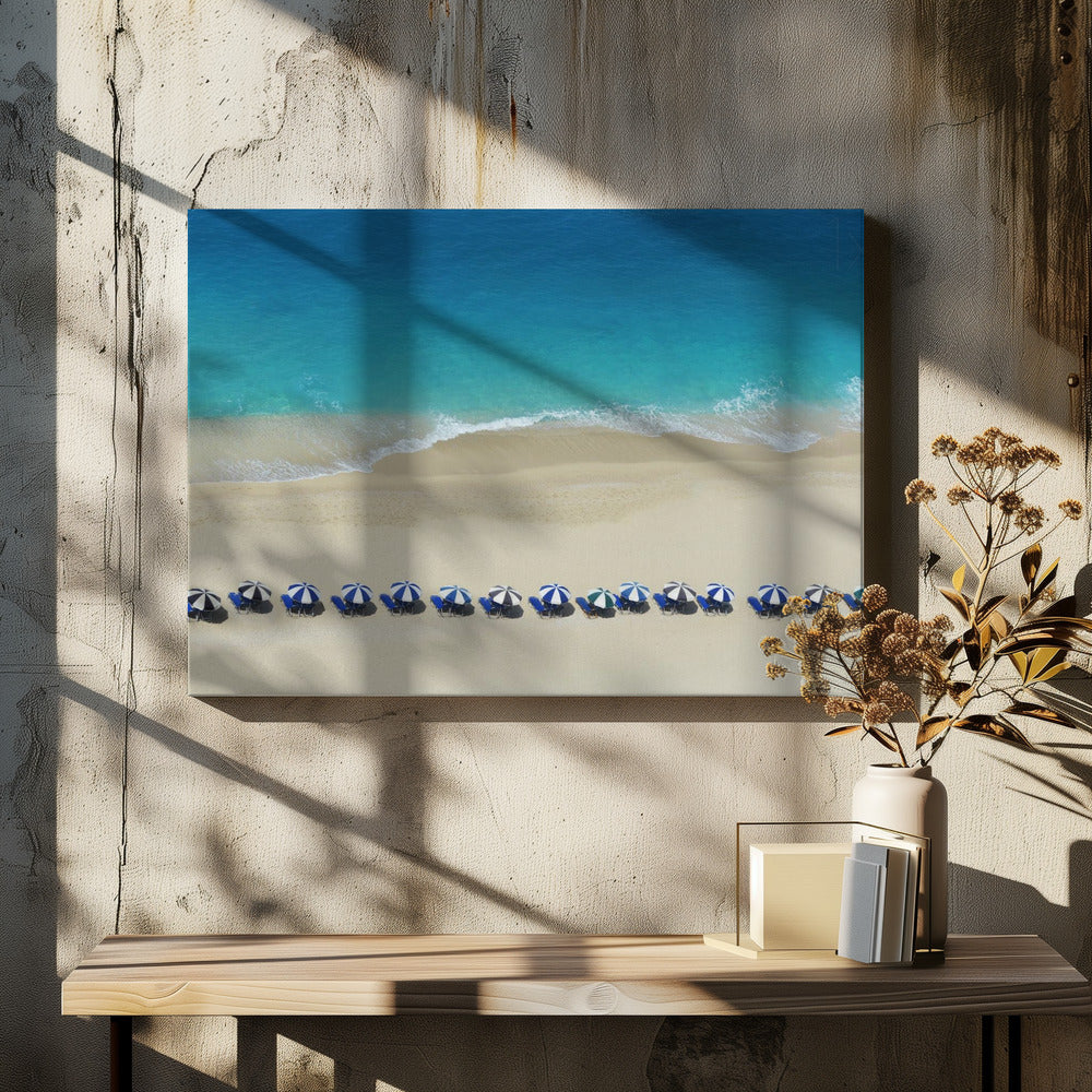 An aerial view of a pristine sandy beach with vibrant turquoise ocean waves gently lapping the shore. A long, neat row of blue and white striped beach umbrellas stands along the sand, creating a serene and orderly coastal scene, all enclosed within a silver frame. Artwork
