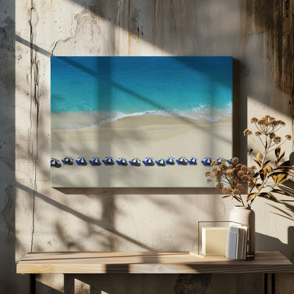 An aerial view of a pristine sandy beach with vibrant turquoise ocean waves gently lapping the shore. A long, neat row of blue and white striped beach umbrellas stands along the sand, creating a serene and orderly coastal scene, all enclosed within a silver frame. Artwork