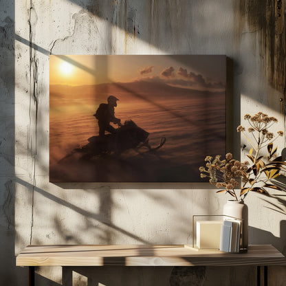 A silhouette of a person wearing a helmet and backpack stands on a snowmobile in a vast, snowy landscape during a golden sunset. The wind blows snow across the ground, creating a hazy, atmospheric effect, with mountains visible in the distance under a warm sky. Wall Art