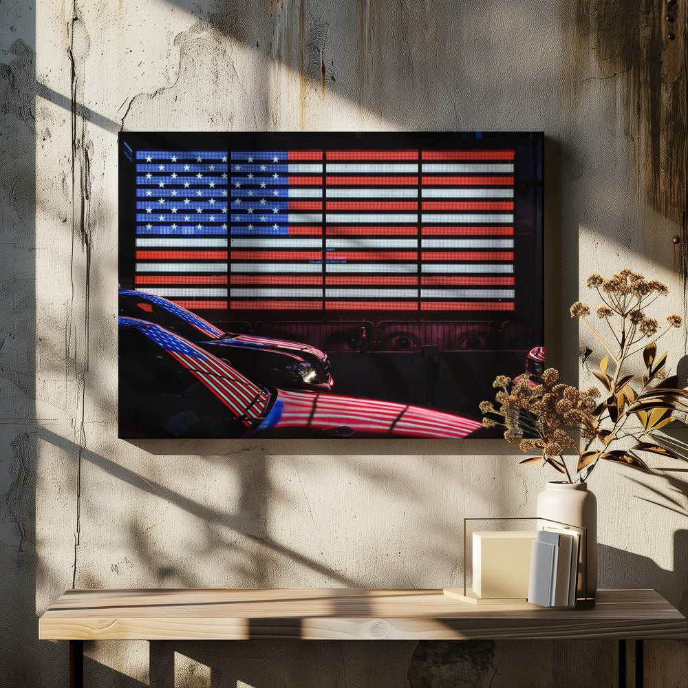A large illuminated American flag on a billboard at night, with its red, white, and blue lights reflecting on the glossy hoods of two cars in the foreground. Wall Art
