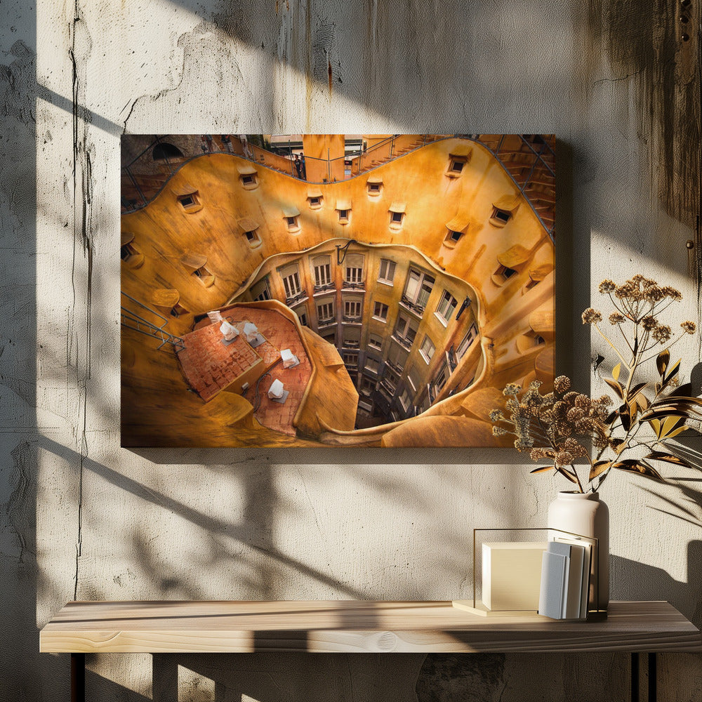 A high-angle photograph looking down into the surreal, undulating inner courtyard of an architectural masterpiece. The warm, golden-ochre walls curve organically, dotted with small, hooded windows, encircling the deep central lightwell that reveals floors of apartments below. Wall Art
