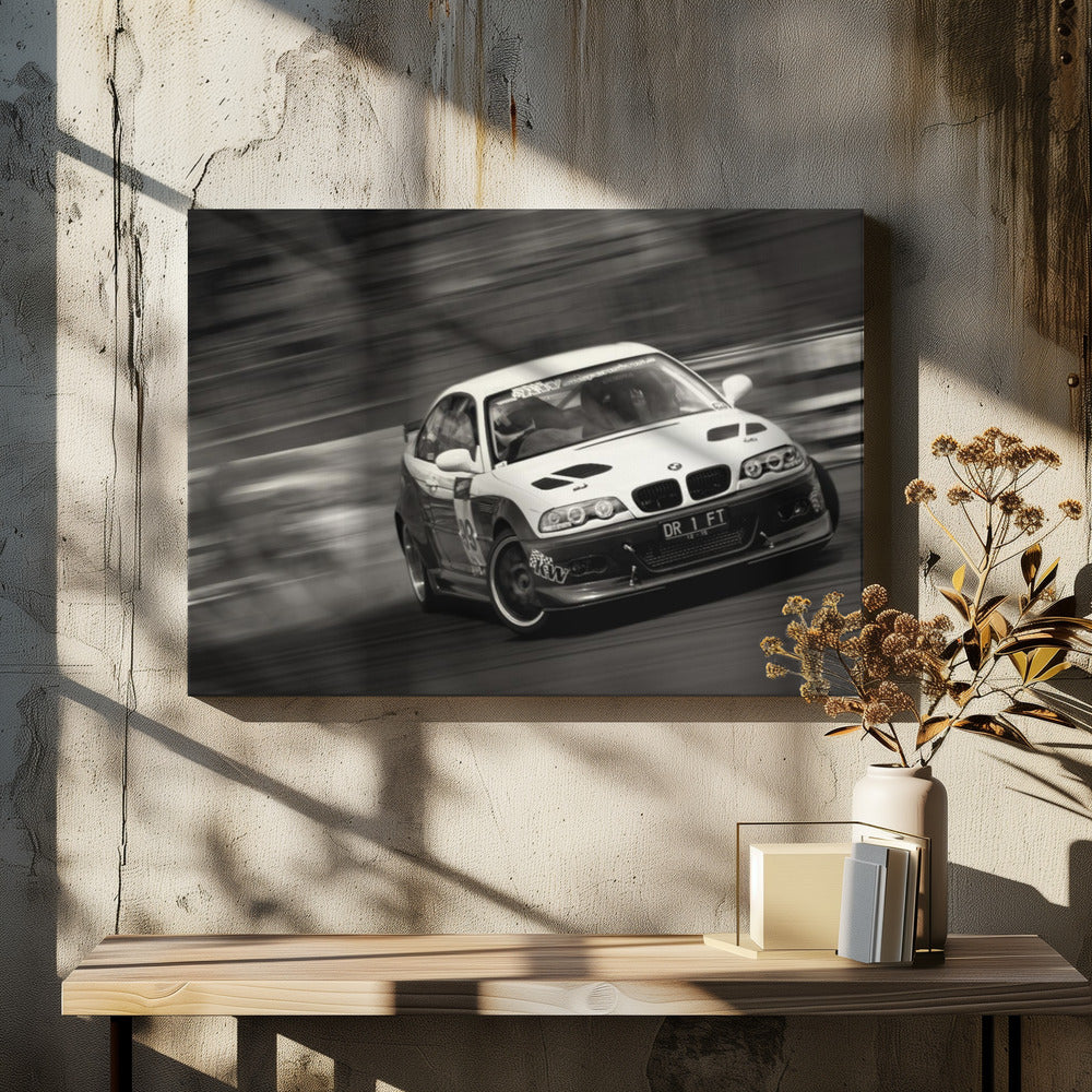 A framed, black and white action photograph of a white and black BMW race car drifting at high speed around a corner. The background is blurred with motion lines, emphasizing the car's speed as it turns, and a puff of smoke is visible from the tires. Wall Art