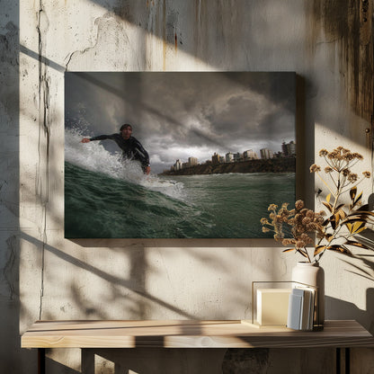 A close-up, low-angle shot of a male surfer in a black wetsuit riding a dark green ocean wave. In the background, a city skyline sits atop a cliff under a dramatic, dark, and stormy sky. The image is presented within a silver picture frame. Print