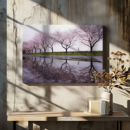 A framed photograph of a row of pink cherry blossom trees on a grey, overcast day, perfectly reflected in a large puddle on a wet road. A small figure of a person is seen running along the grassy bank in the distance. Poster