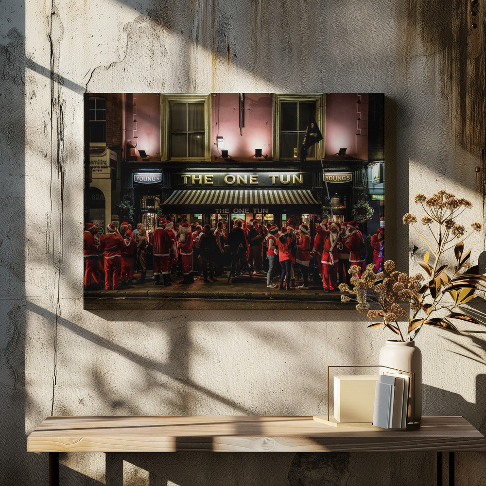 A nighttime photograph of a large crowd of people dressed in Santa Claus costumes standing outside a warmly lit pub called 'The One Tun', creating a festive holiday atmosphere on a city street. Print