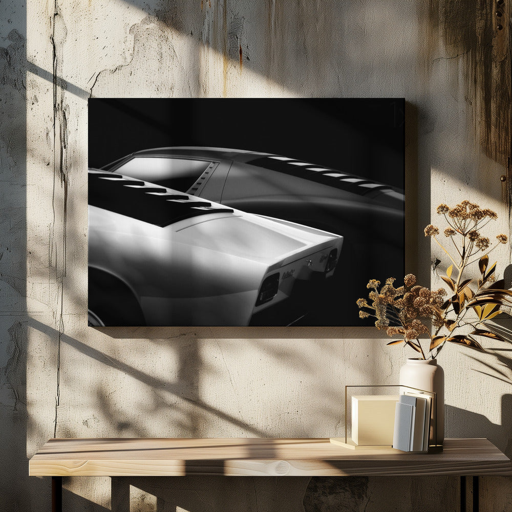 A dramatic black and white studio photograph showcasing the sleek, curved lines of two classic sports cars, with a white car in the foreground and a dark one in the background, set against a black backdrop. Wall Art