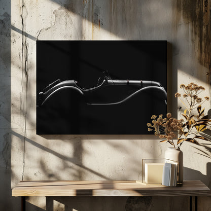 A dramatic black and white photograph showcasing the elegant silhouette of a vintage roadster. The side profile of the classic car is highlighted by subtle light, emphasizing its long hood and sweeping fenders against a solid black background, all within a brushed silver frame. Print