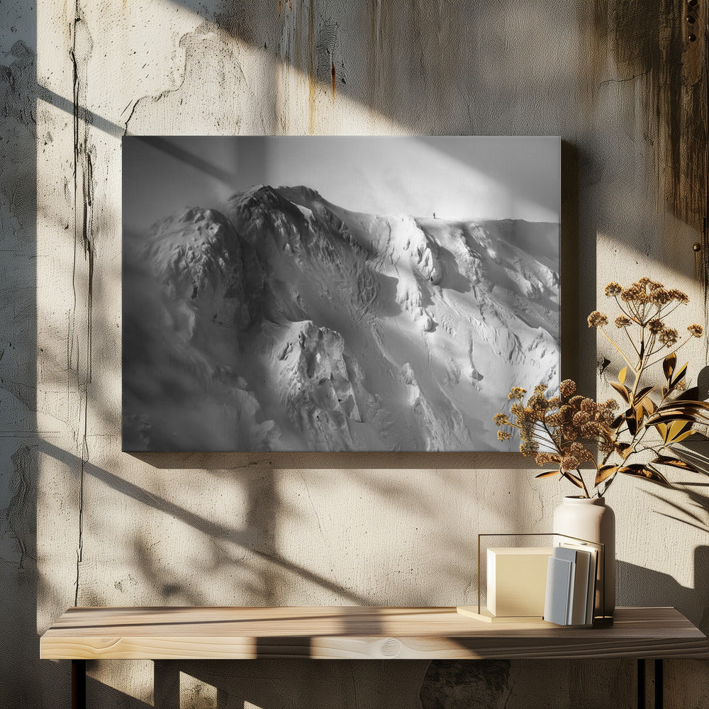 A dramatic black and white photograph of a person standing alone on the ridge of a massive, snow-covered mountain, emphasizing the scale and solitude of the vast, rugged landscape, all presented in a silver frame. Wall Art