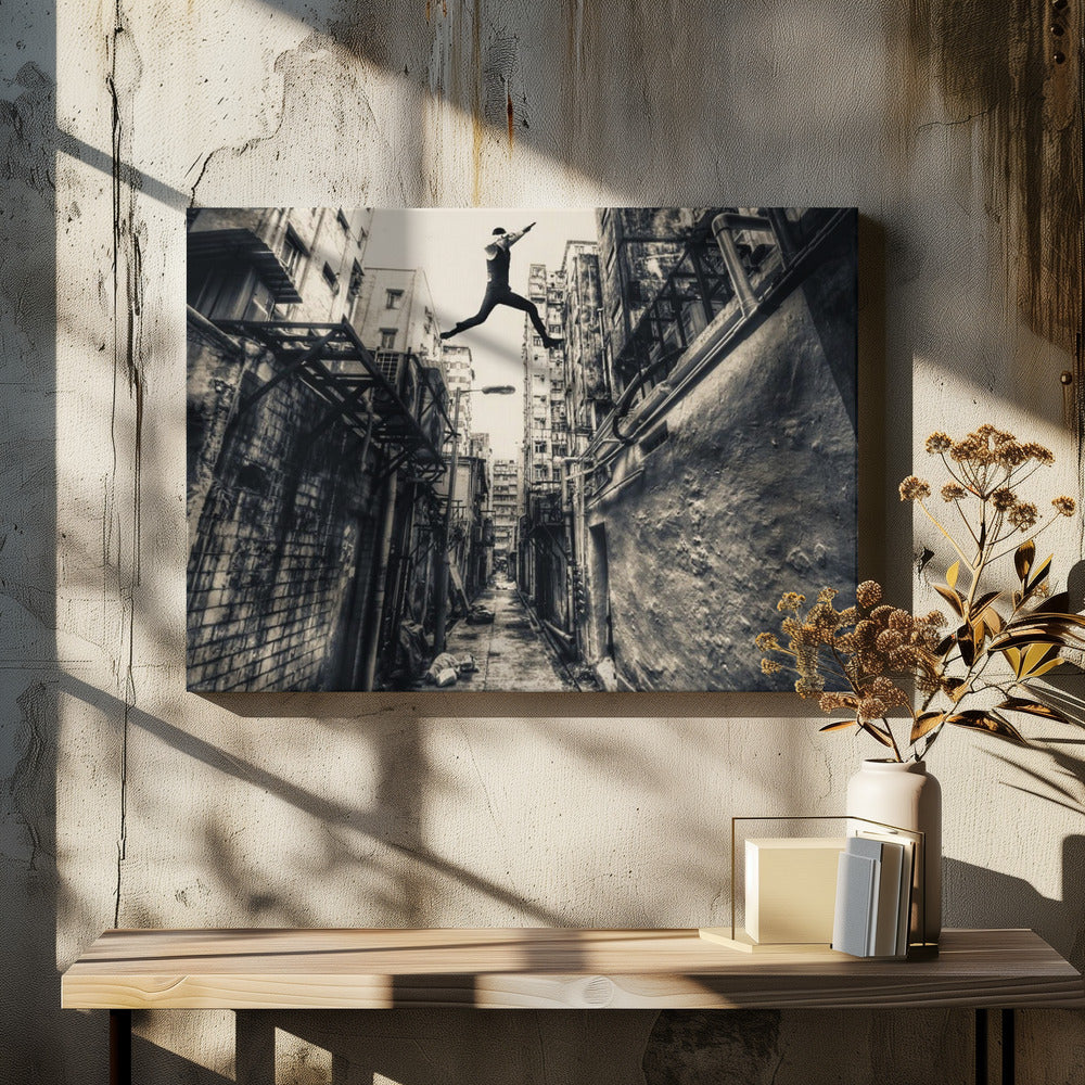 A dramatic black and white photograph of a man in mid-air, leaping athletically across a narrow, gritty urban alleyway. The low-angle shot looks up between tall, weathered buildings, emphasizing the height of the jump. The image is presented in a silver frame. Wall Art