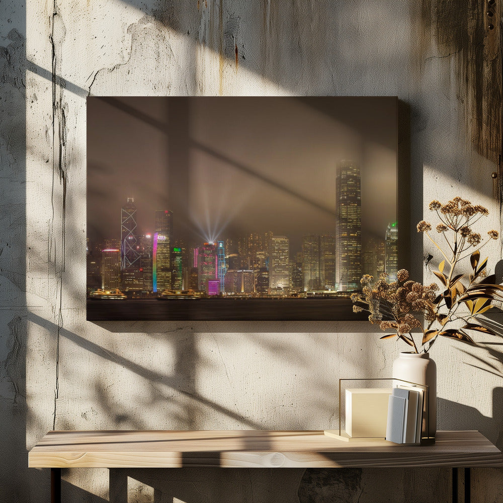 A framed photograph of the Hong Kong skyline at night, viewed from across the water. The skyscrapers are brilliantly lit with yellow, white, and colorful lights, and beams of light shoot up into the foggy, glowing sky. Decor