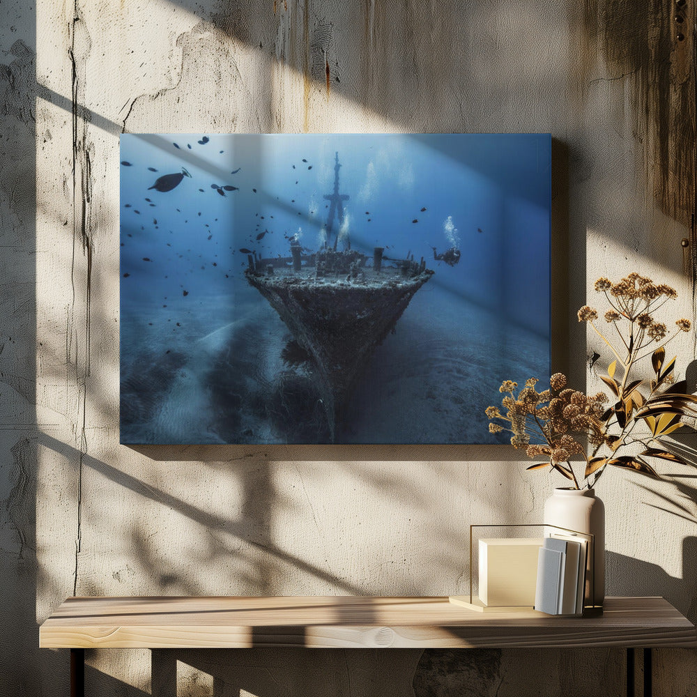 An underwater photograph of a large, sunken shipwreck resting on the sandy ocean floor. Two scuba divers are exploring the wreck, surrounded by schools of small fish in the deep blue water, with light filtering down from the surface. Print