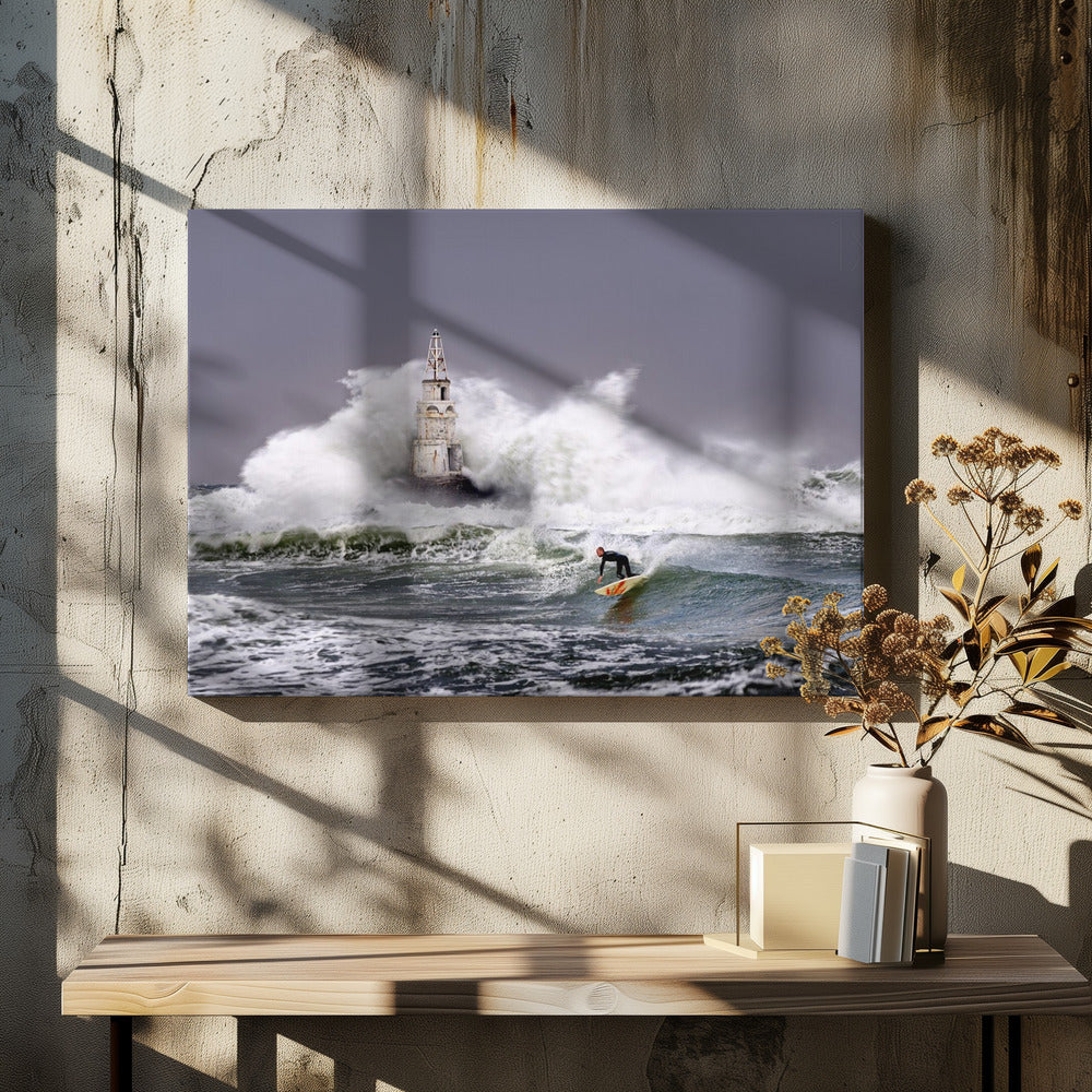 A framed photograph of a surfer in a black wetsuit riding a wave in a stormy sea. In the background, massive white waves crash against an old white lighthouse under a grey, overcast sky. Artwork
