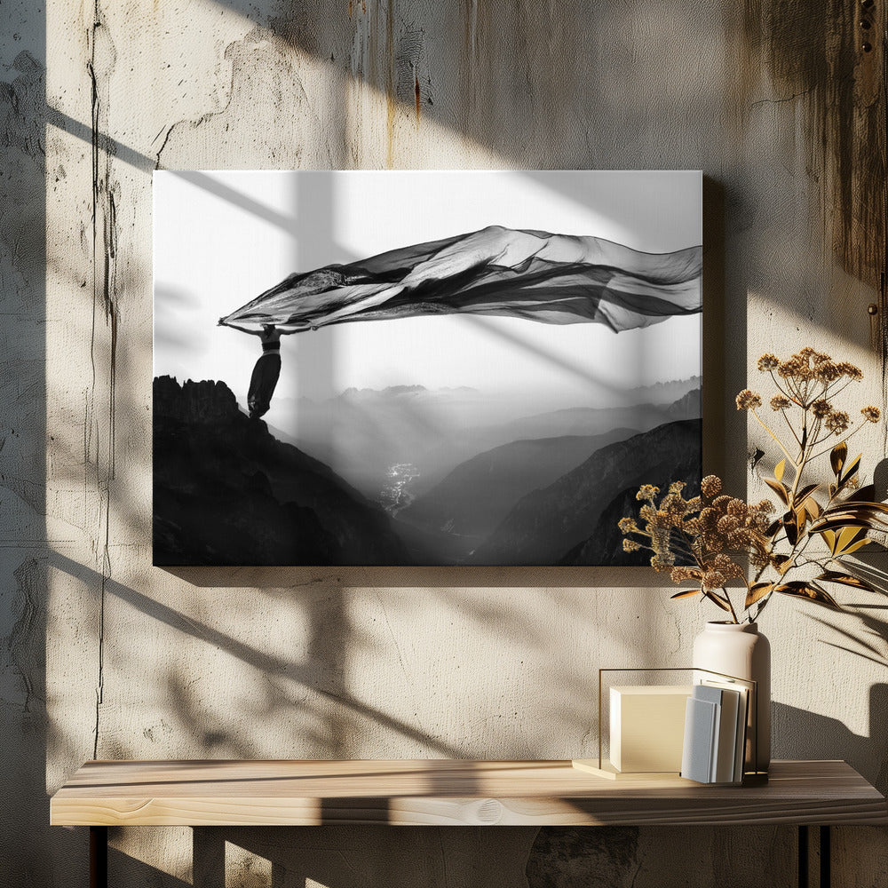 A dramatic black and white photograph of a woman standing on the edge of a mountain peak. She holds up a massive piece of dark, sheer fabric that billows in the wind, stretching across the sky. Below her, a vast, misty mountain range and a deep valley with city lights are visible. Wall Art